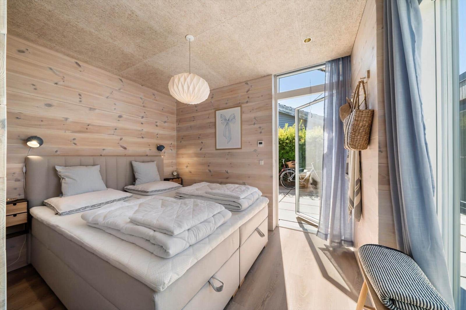 Bedroom with wooden wall, bed, and view of terrace.