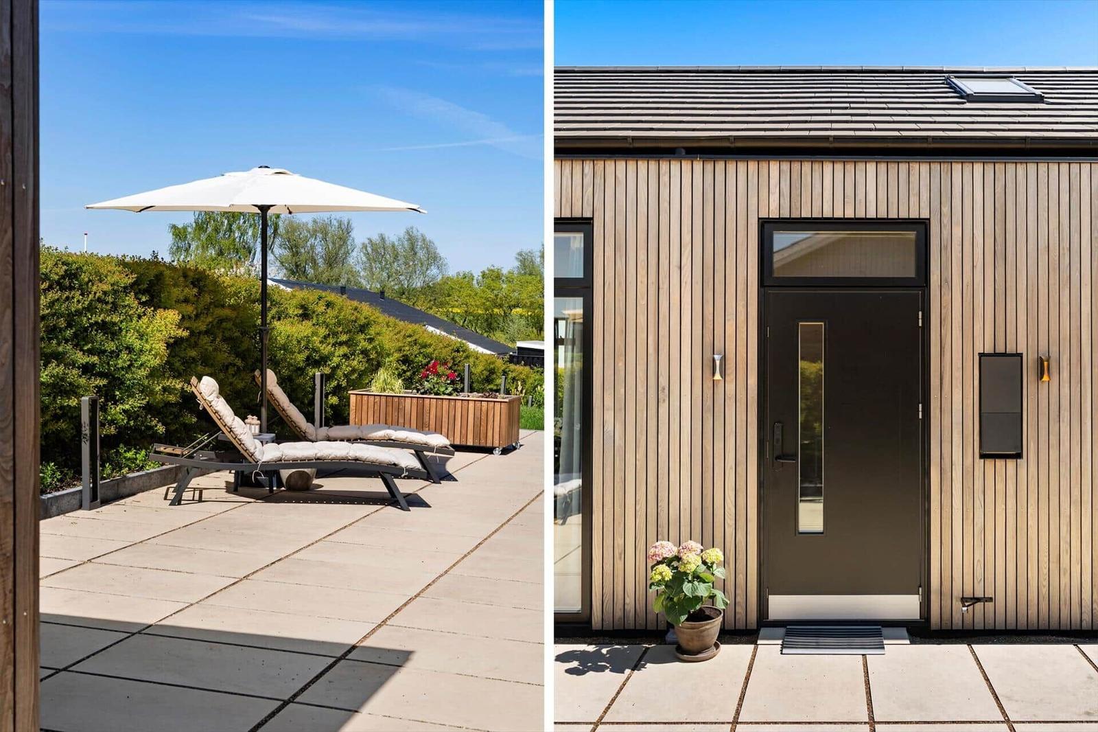 Terrace with loungers and umbrella. Entrance with wooden cladding and door.