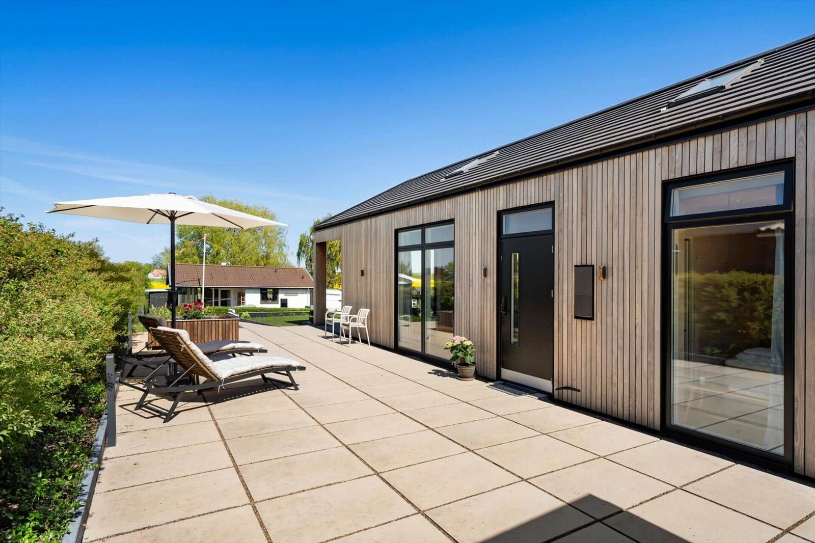 Modern wooden house with large terrace and sun protection.