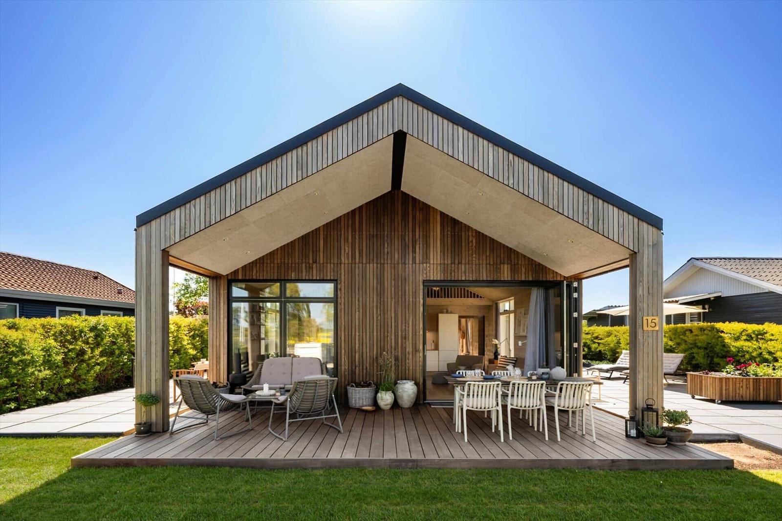 Modern wooden cabin with covered deck, seating, and view into the kitchen.