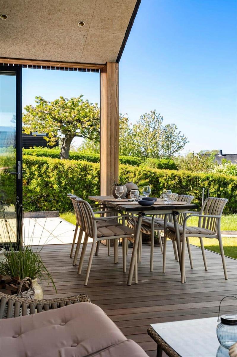 Deck with table and chairs, view of green hedge and tree.