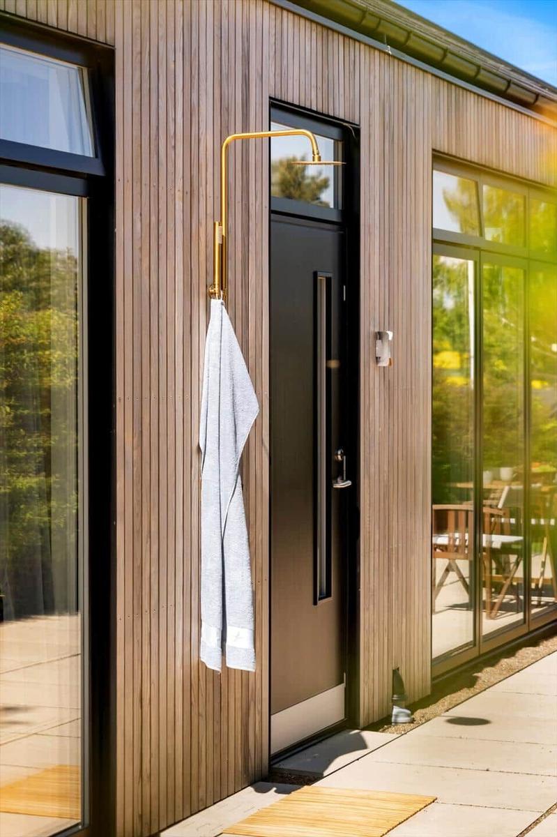 Outdoor area with black door, gold shower, and towel on wooden wall.