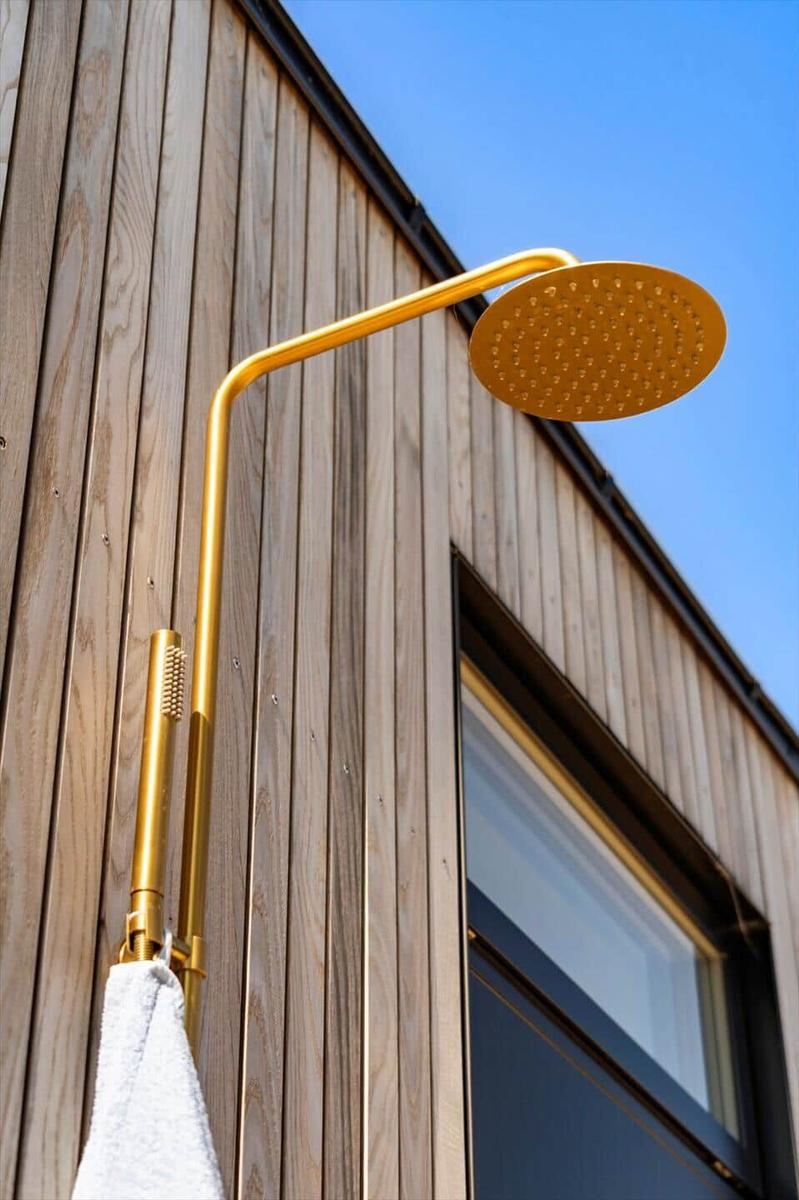 Gold showerhead on wooden wall with window in background.