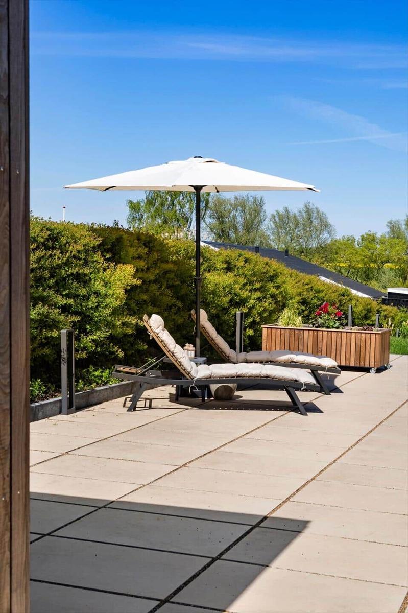 Terrace with lounge chairs and umbrella. Background: green hedge and blue sky.