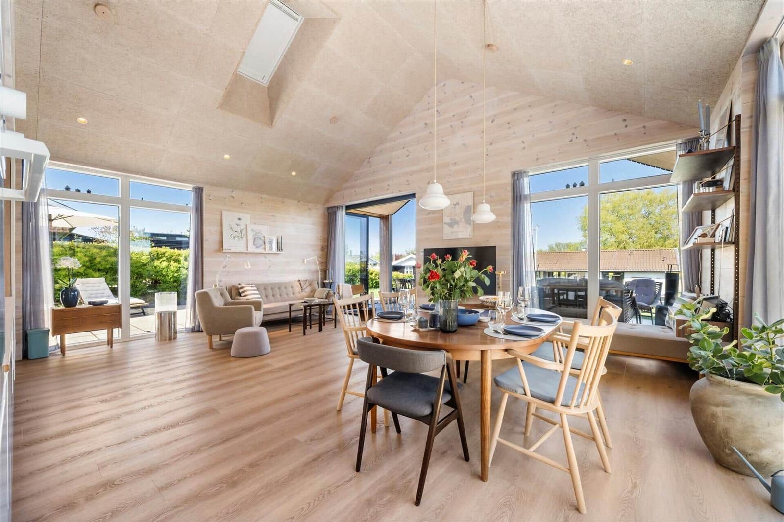 Spacious room with wooden ceiling, dining table, and large windows. View of garden and terrace.