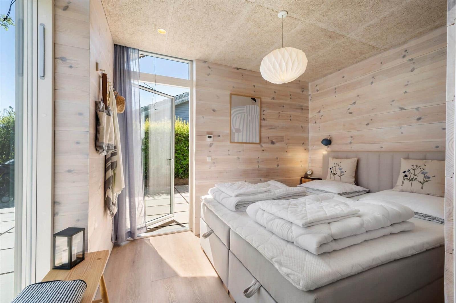 Bedroom with wooden walls, bed, and window to terrace.