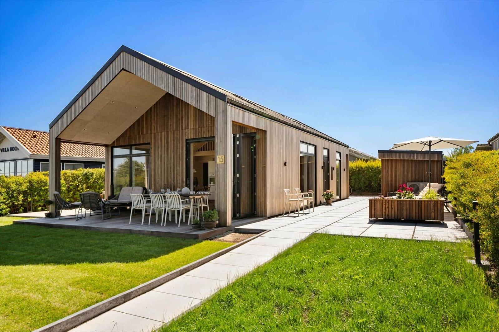 Modern villa with wooden facade, terrace, and garden. Outdoor table, seating, and sunshade.