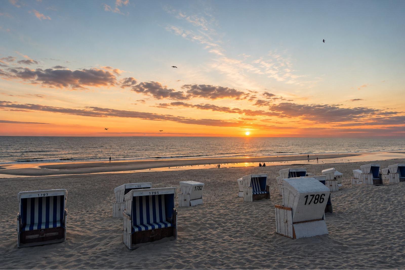Strand mit Strandkörben und Sonnenuntergang über dem Meer.