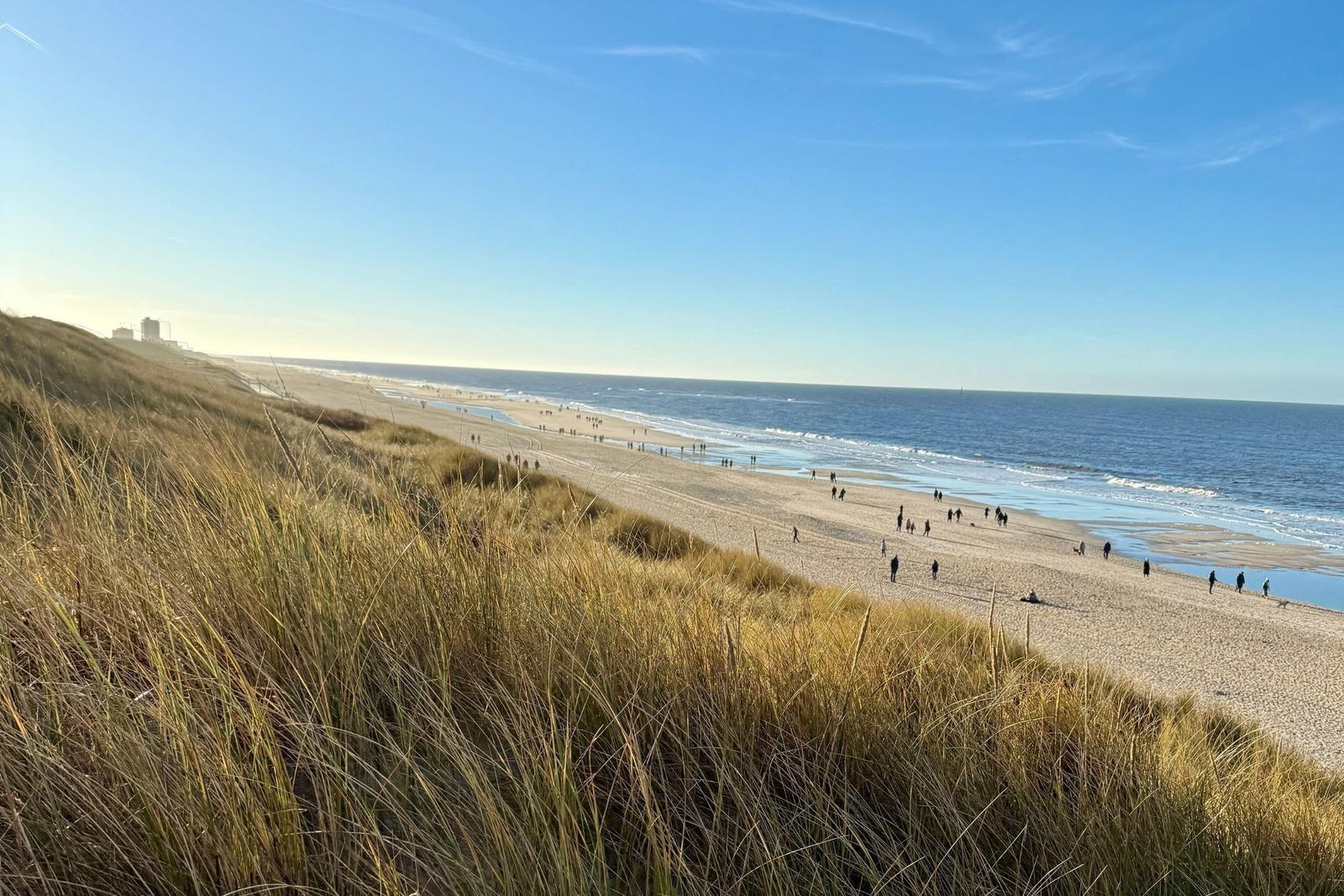 Strand mit Dünen und Menschen. Blick auf das Meer unter blauem Himmel.