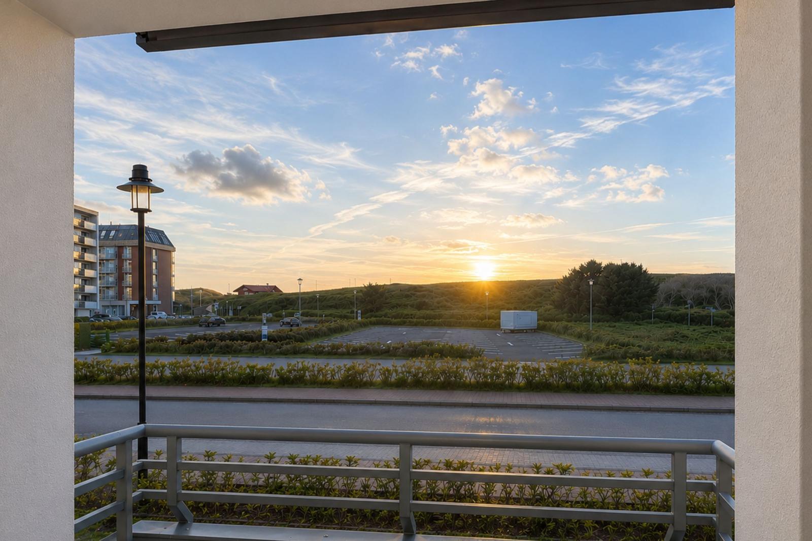 Blick vom Balkon auf Sonnenuntergang, Straße, Parkplatz und Grünfläche.