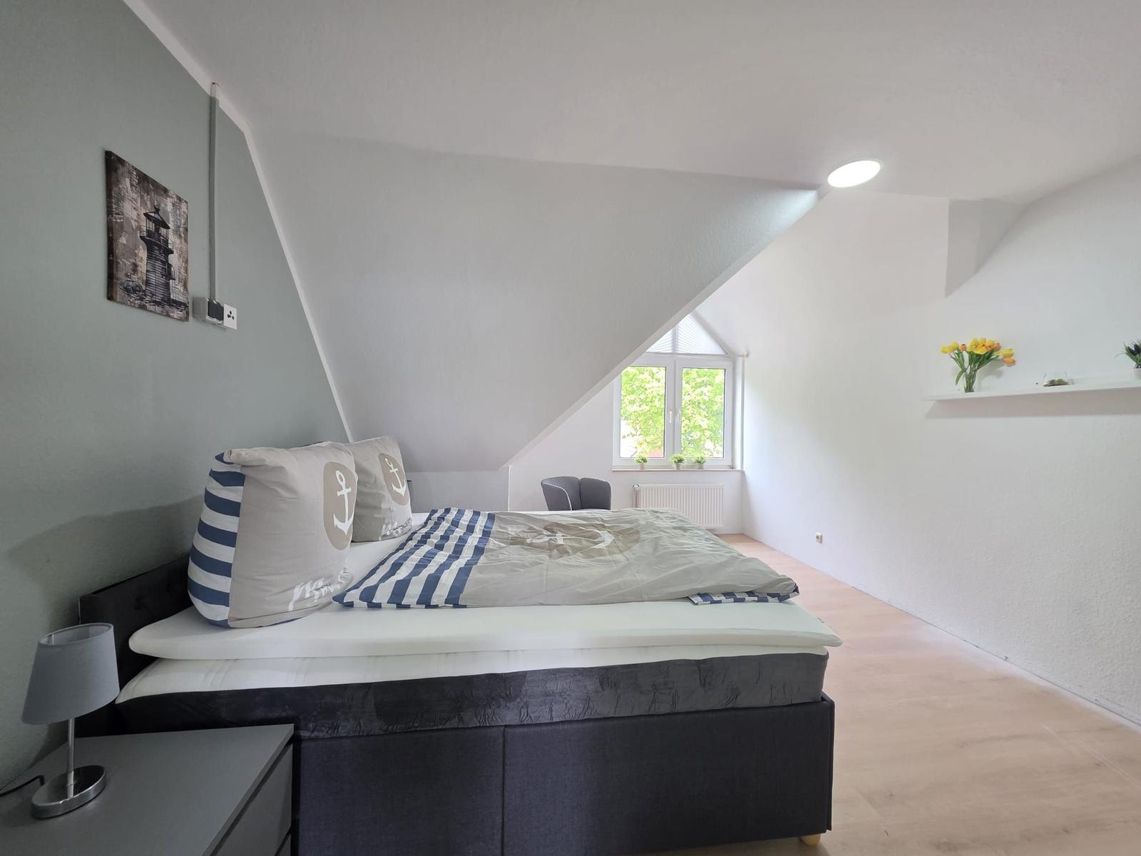 Bedroom with sloped ceiling, bed with nautical bedding, window, and desk.