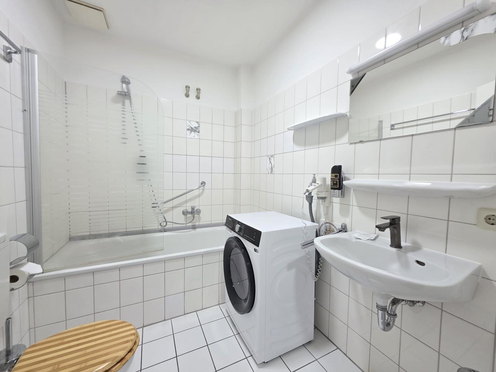Bathroom with bathtub, shower, washing machine, and sink.