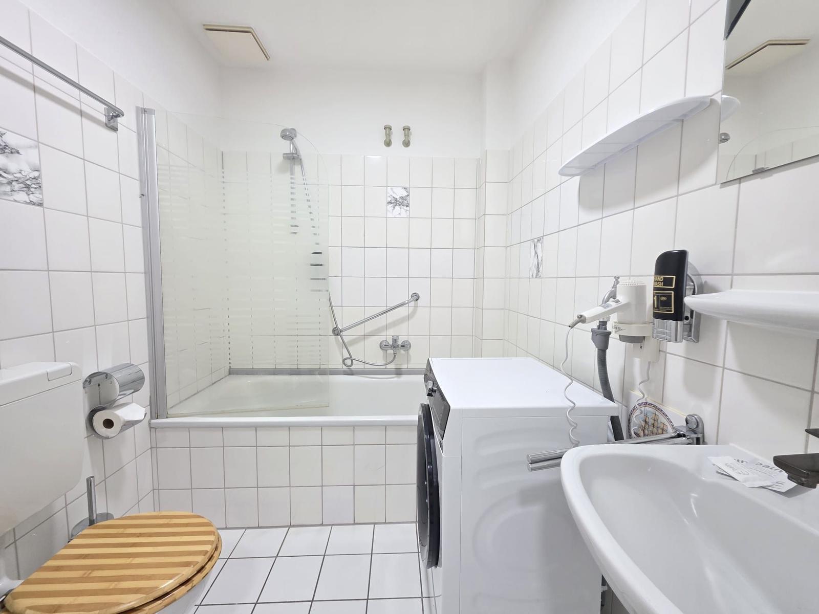 Bathroom with bathtub, shower, washing machine, and sink.
