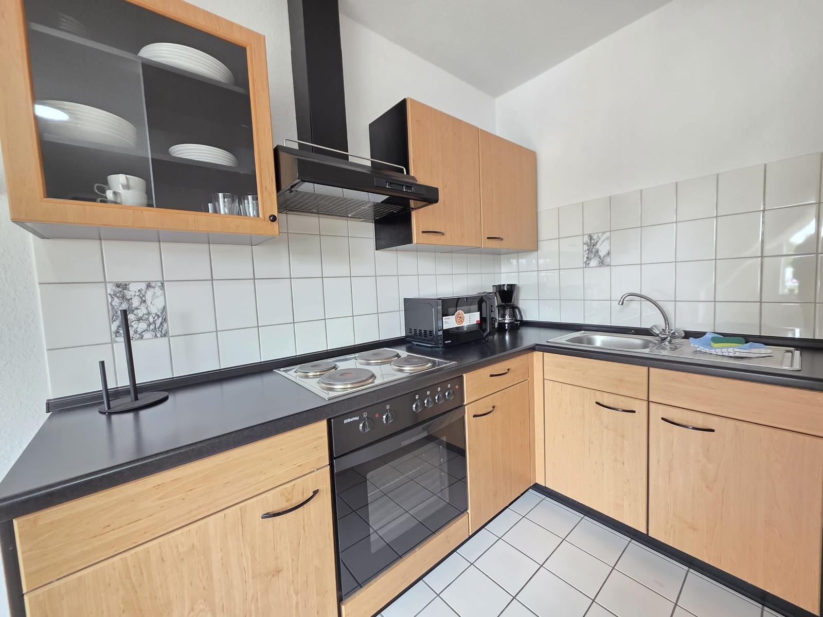 Kitchen with wooden cabinets, stainless steel sink, and cooktop with oven.