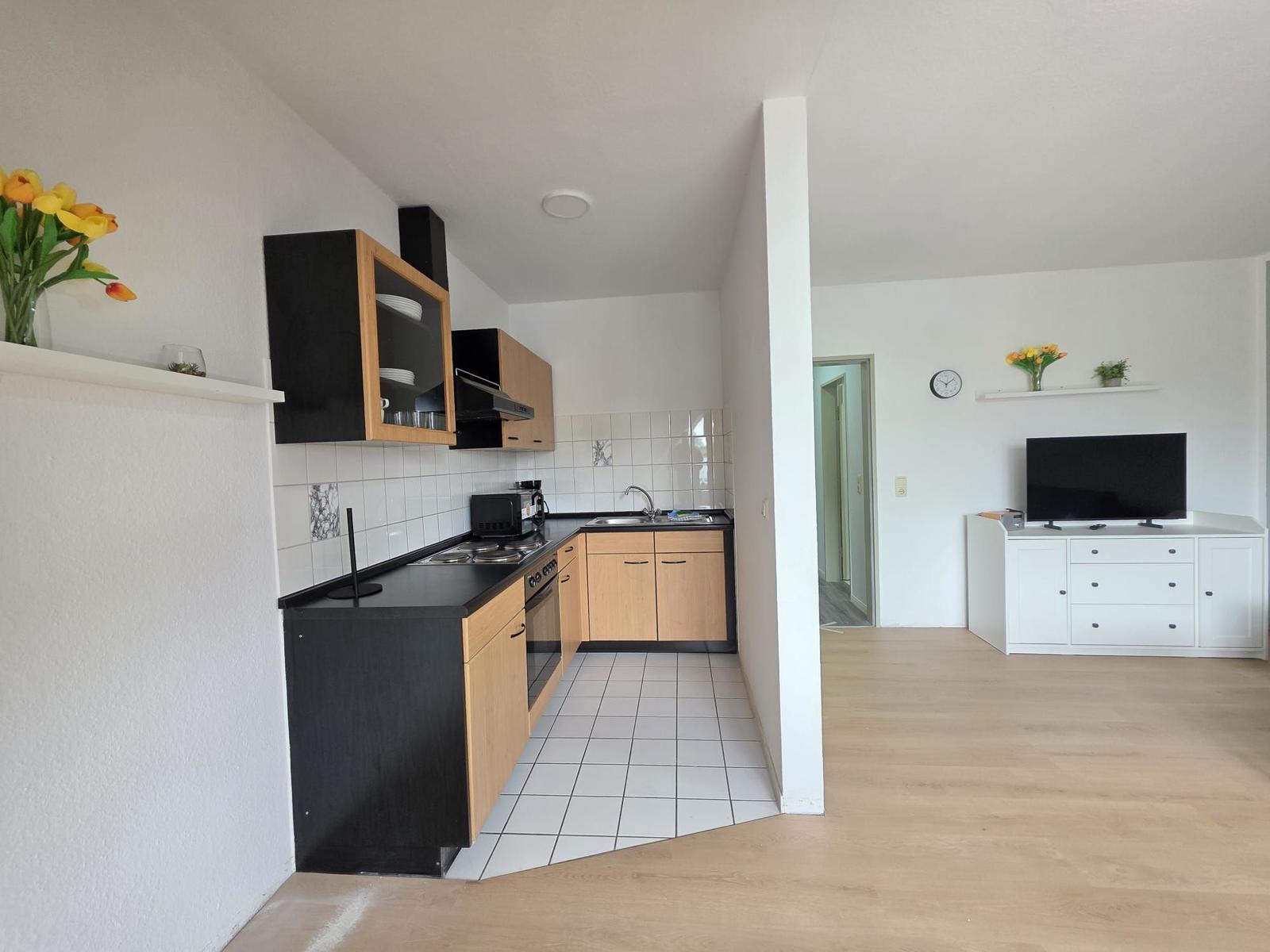 Kitchen with wooden cabinets and countertop. Living room with TV and cabinet.