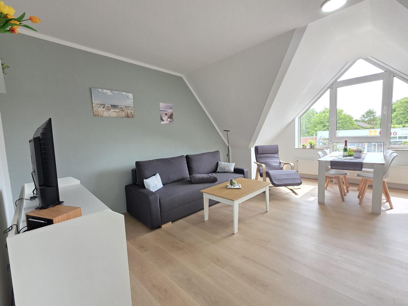 Living and dining area with sofa, dining table, and large window. Wooden floor and gray walls.