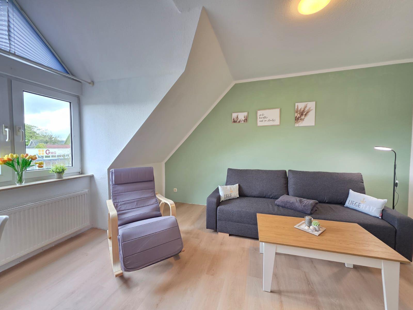 Living room with sofa, chair, table, and window. Green wall, wooden floor.