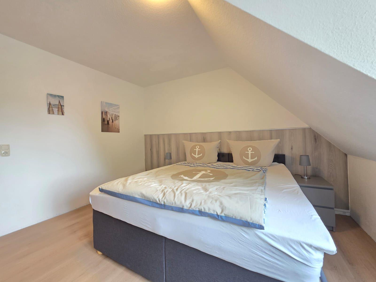 Bedroom with double bed, anchor motif, and wooden wall under sloped ceiling.