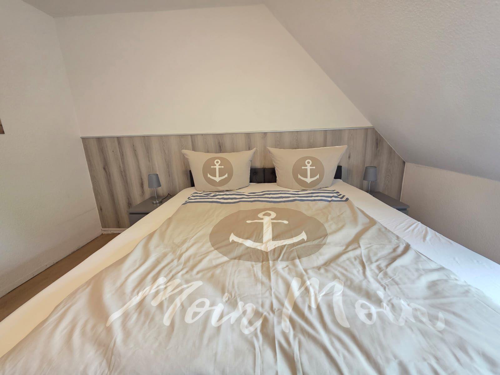 Bedroom with bed, pillows, and bedding featuring anchor motif and Moin Moin text.