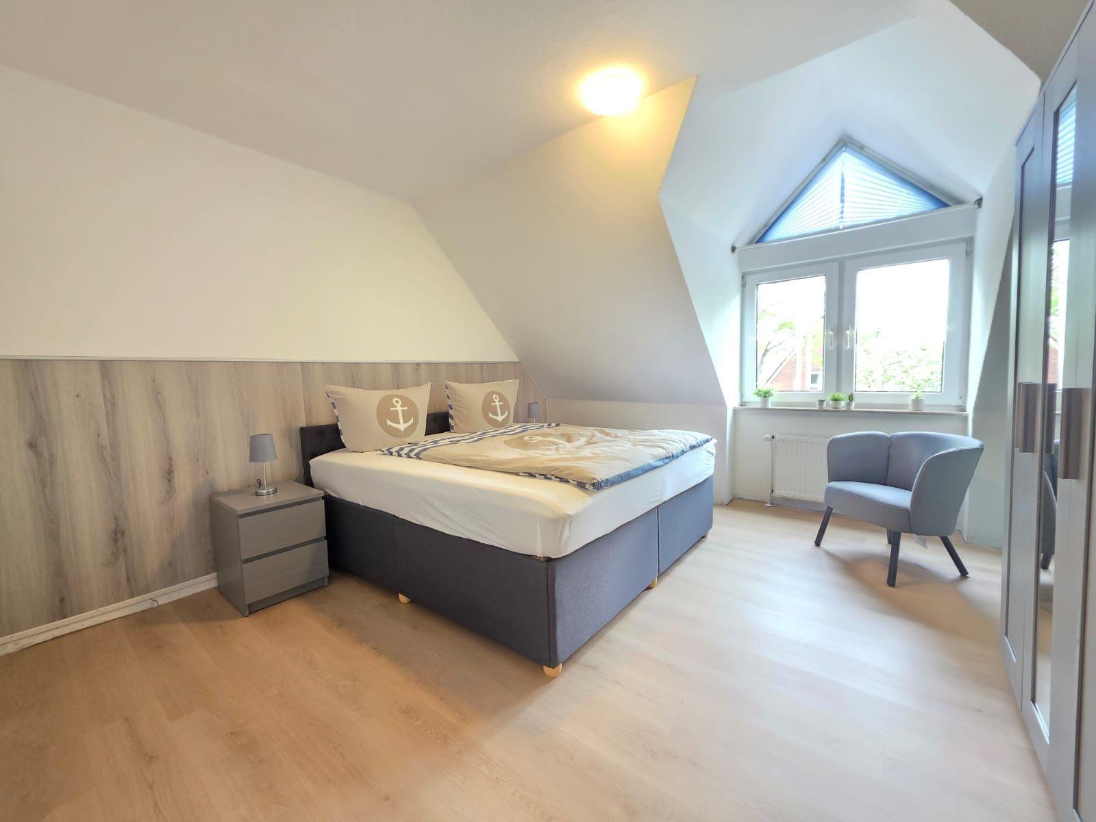 Bedroom with sloped ceiling, bed, nightstand, chair, and window.