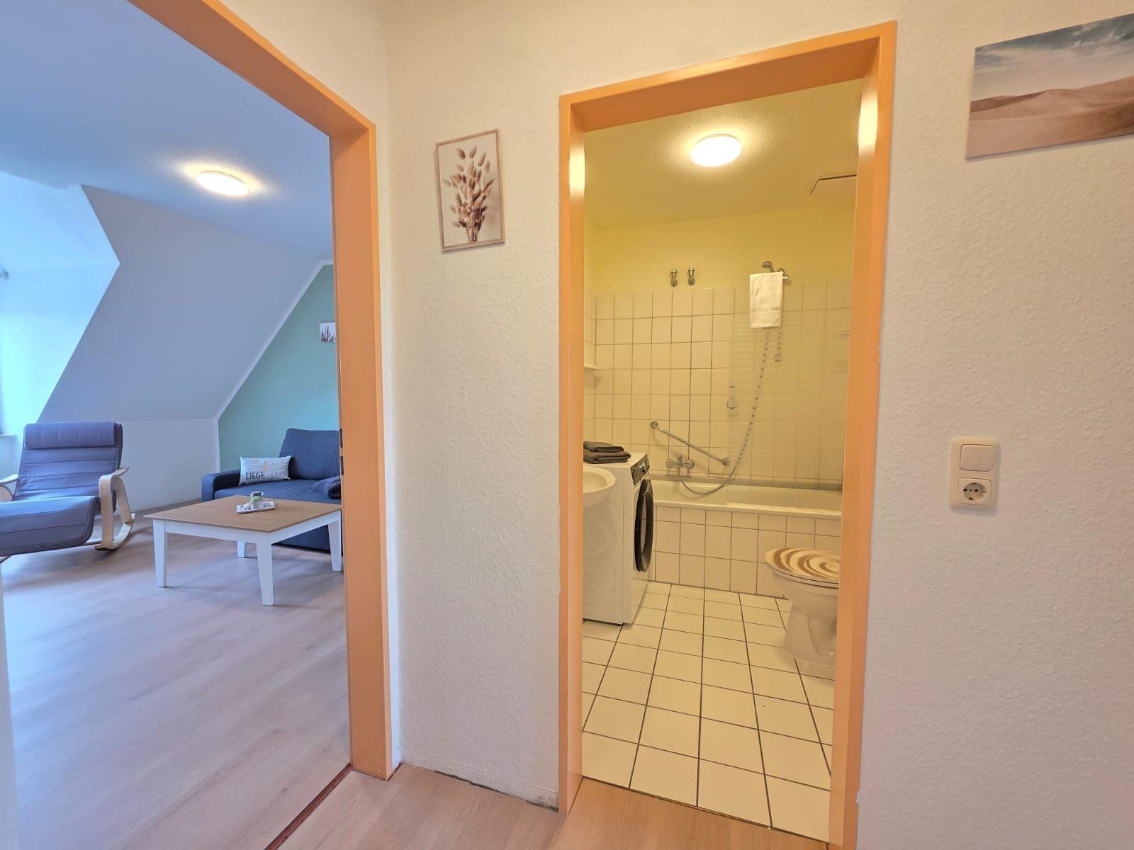 Living area with sofa and coffee table. Adjacent room with bathroom, bathtub, and washing machine.