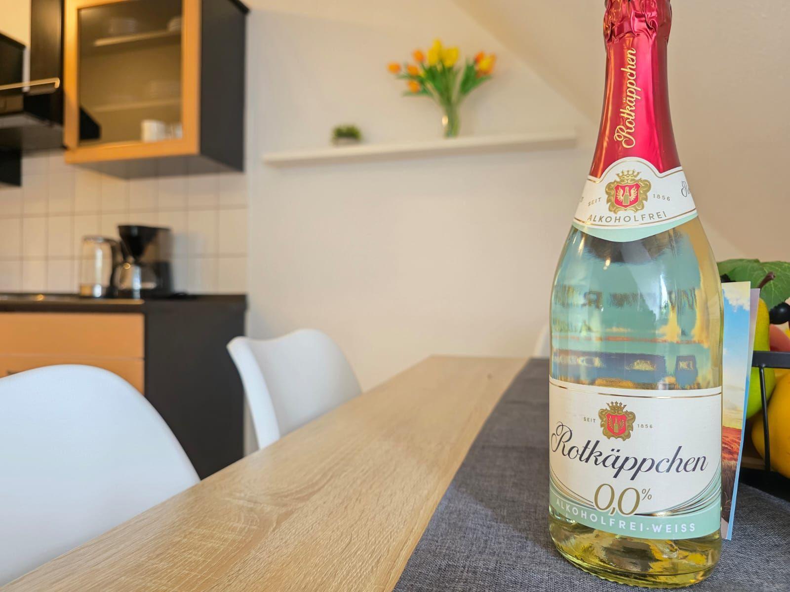 A bottle of alcohol-free white wine sits on a dining table in a kitchen with white chairs.