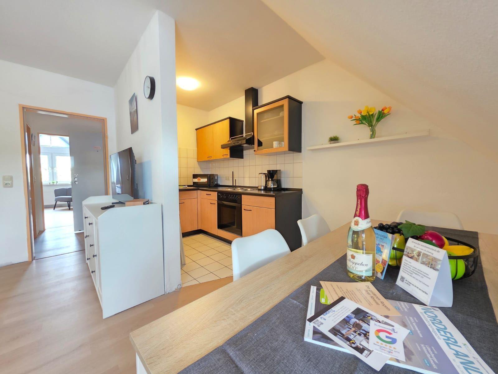 Kitchen with dining area, table with fruit and bottle, TV, and door to living room.