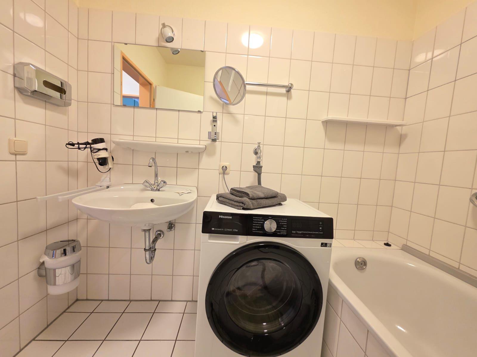 Bathroom with washing machine, bathtub, and mirror on the wall.