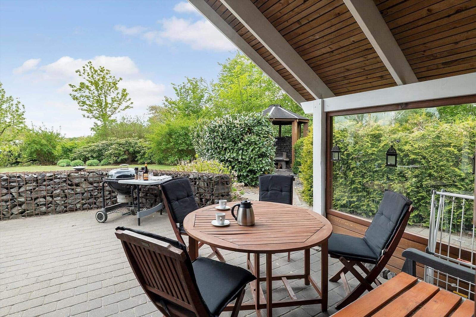 Terrace with table, chairs, grill, and garden view.