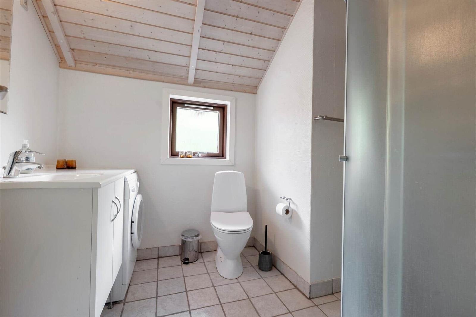 Bathroom with toilet, washing machine, and shower under wooden ceiling.