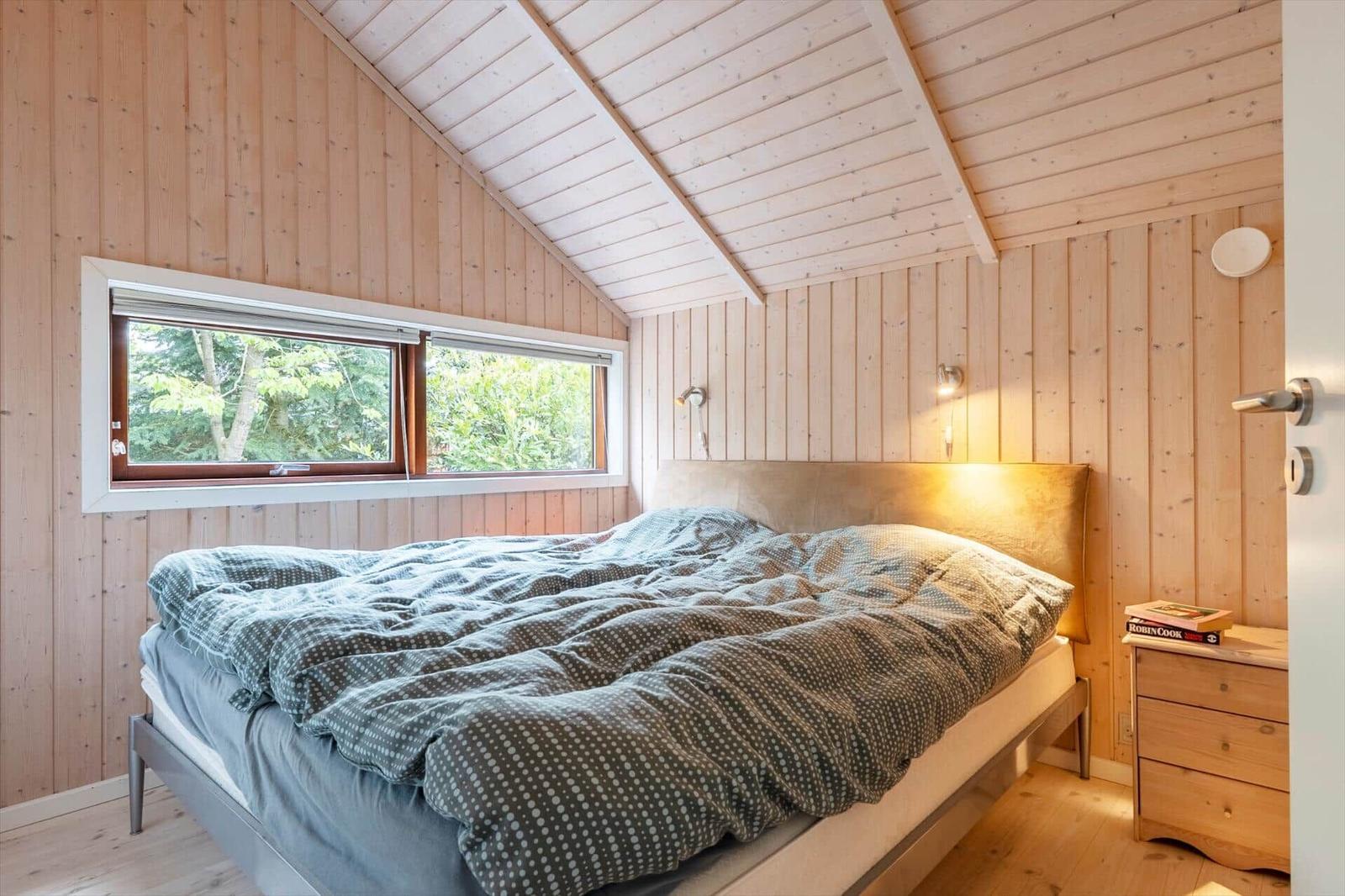 Bedroom with wooden walls, roof window, and bed with cushioned headboard.