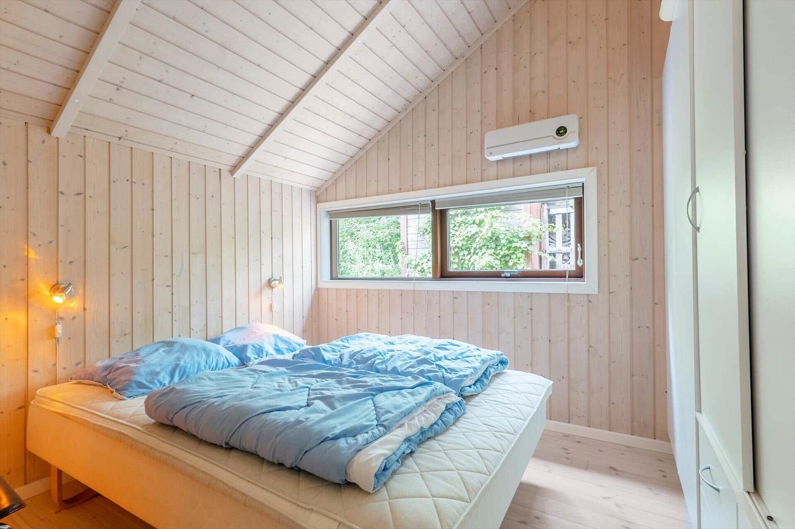 Bedroom with wooden walls, bed, and window. Air conditioner on the wall.