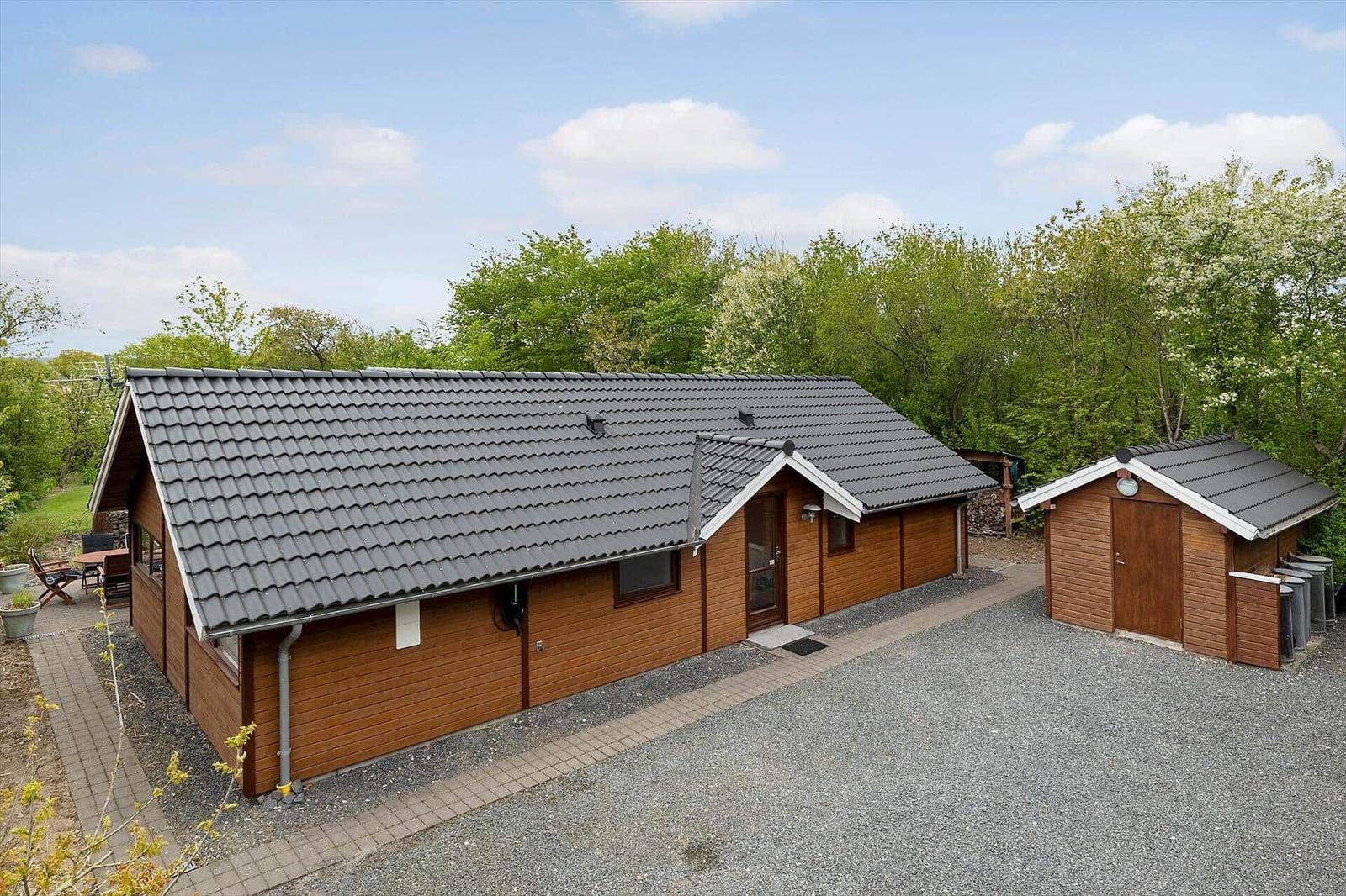 Wooden house with gray roof, garden area, and small garage. Surrounded by trees.