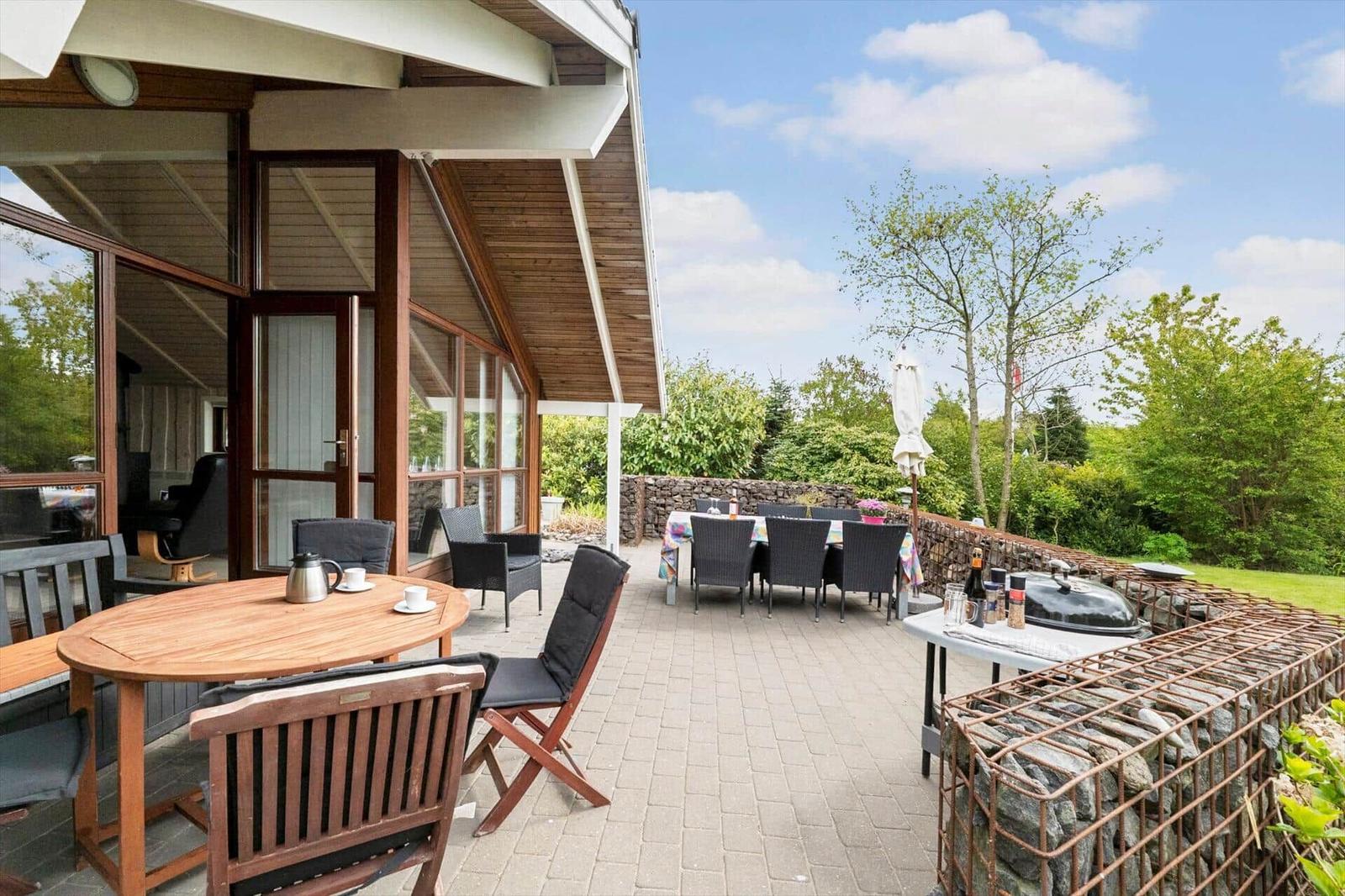Terrace with tables, chairs, and grill. Background: green landscape and house.