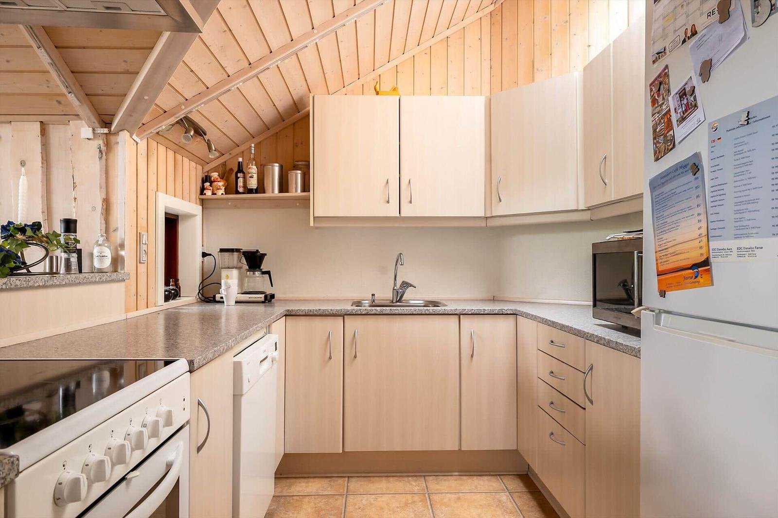 Kitchen with wooden walls, light cabinets, sink, and refrigerator.