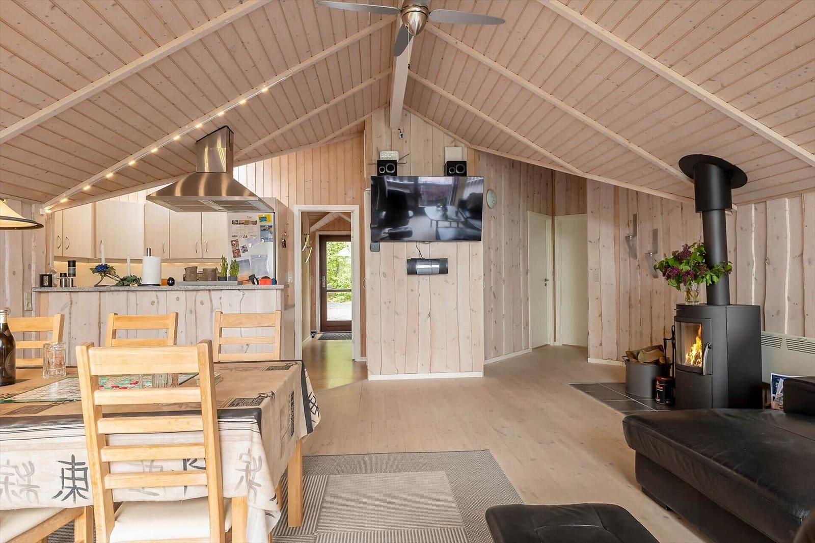 Living area with wooden ceiling, wood stove, TV, and dining table with chairs.