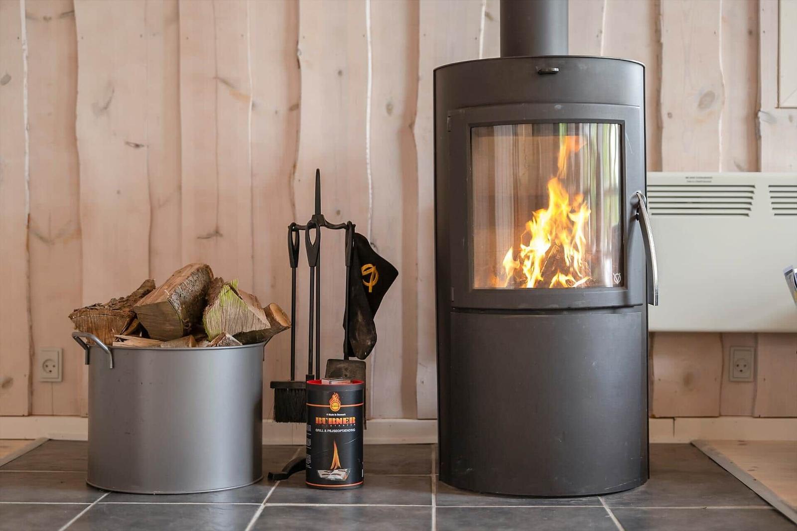 Wood stove with burning fire, next to fireplace tools and firewood in bucket.