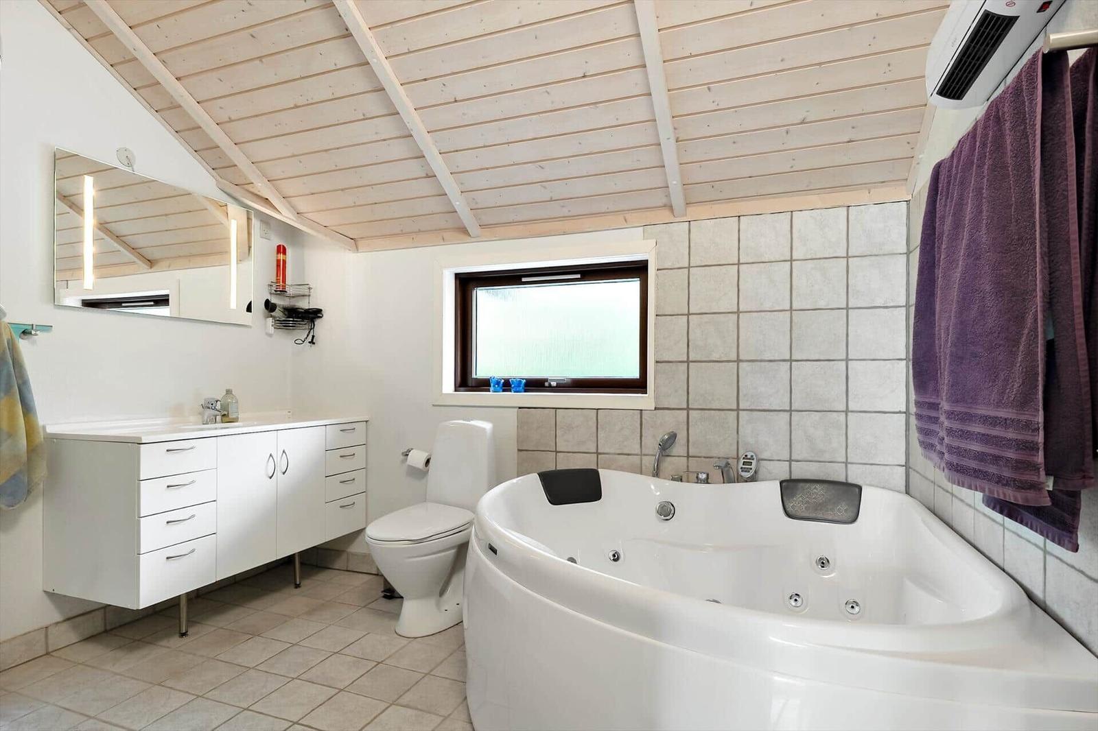 Bathroom with jacuzzi, toilet, and sink under wooden ceiling.