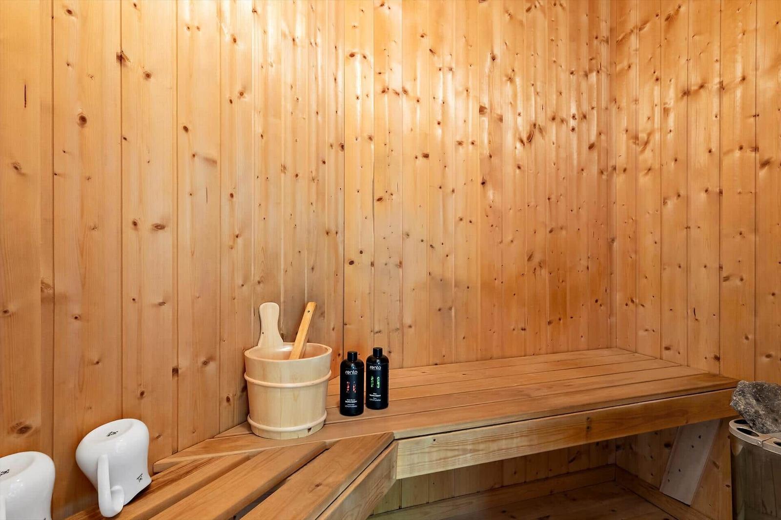 Sauna with wooden walls, bench, and wooden bucket. Two bottles and a wooden bucket are in front.