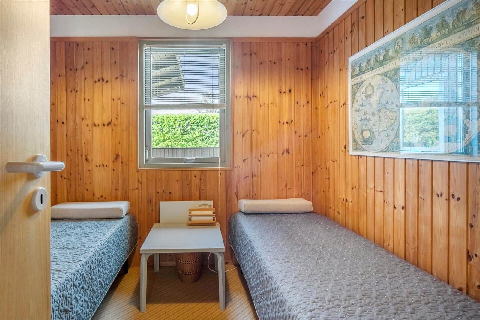 Two beds in a room with wood paneling and a window. An old map hangs on the wall.