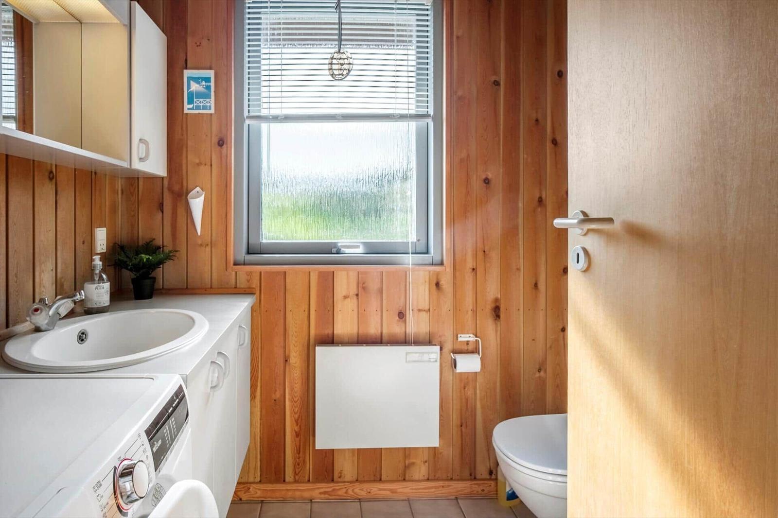 Bathroom with washing machine, toilet, and window with blinds.