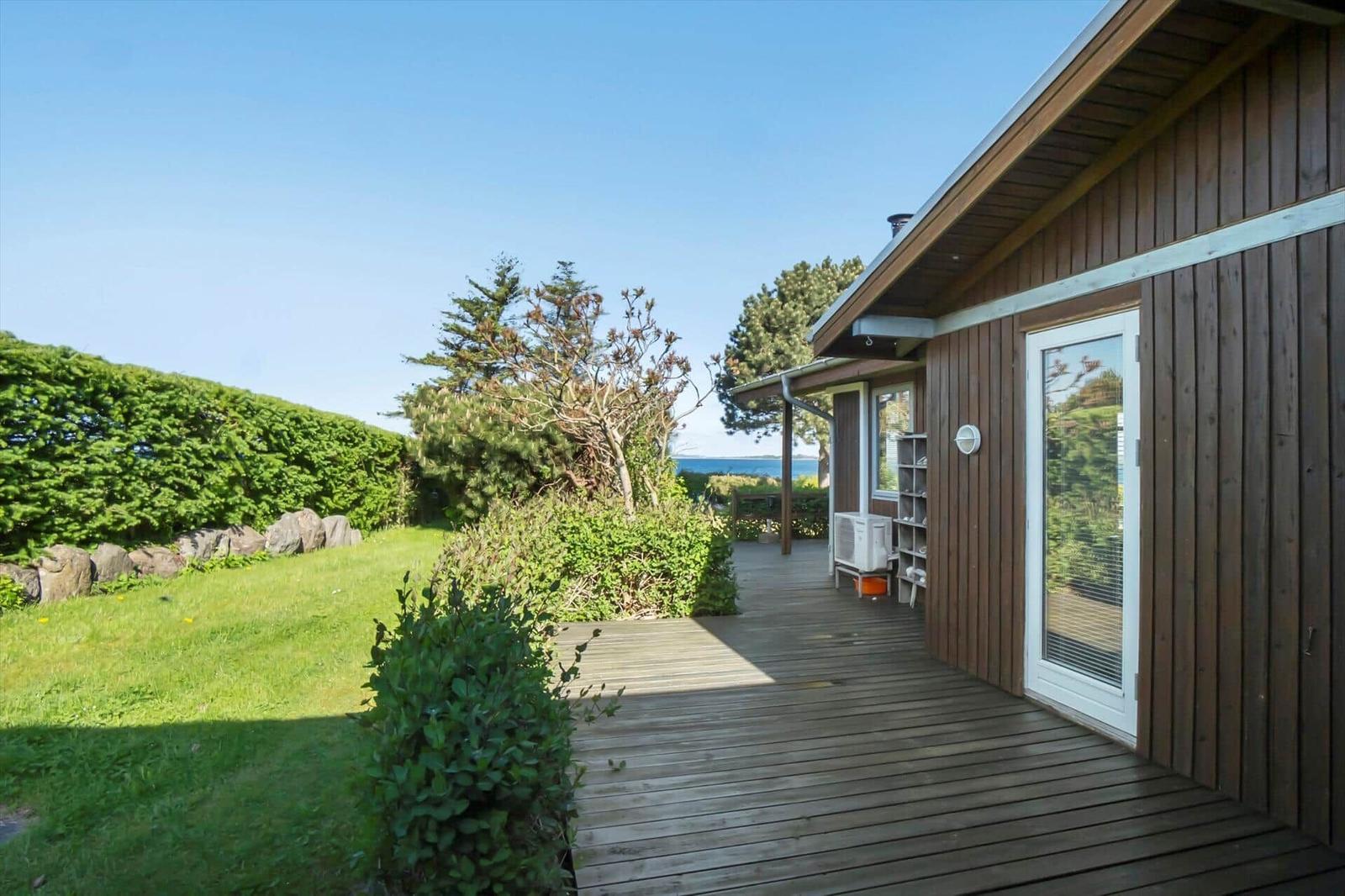 Wooden deck with view of green areas and sea. Entrance door and outdoor area visible.