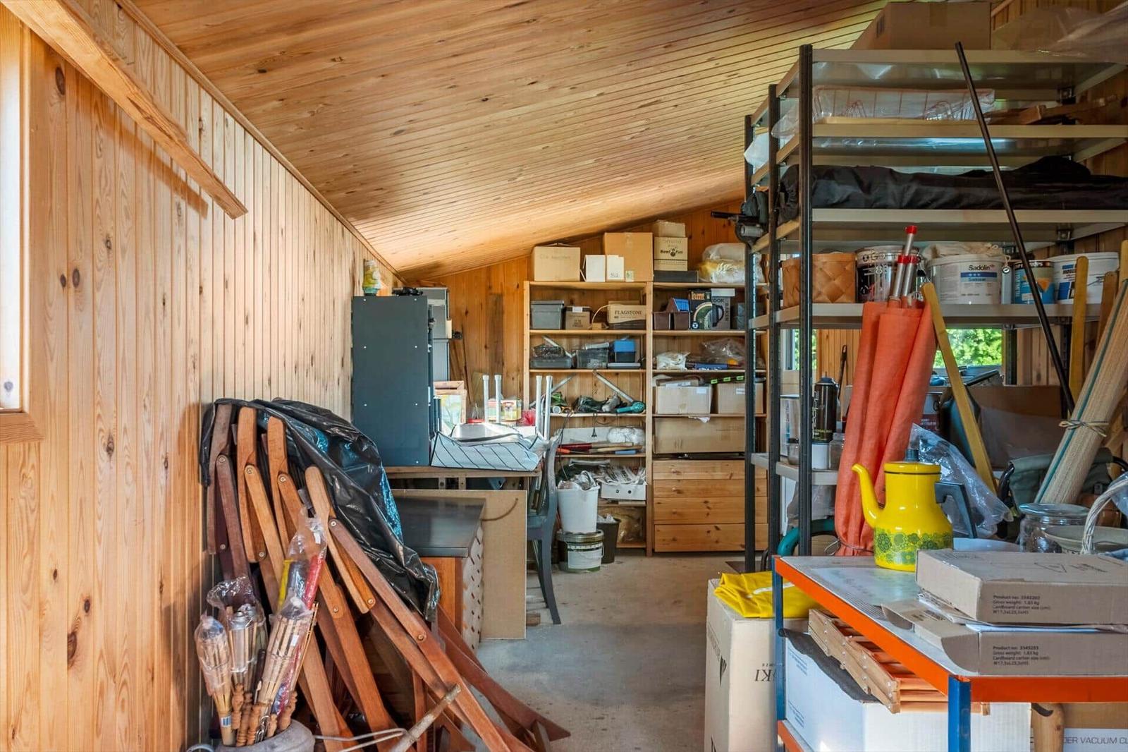Wood-paneled garage with shelves, tools, and boxes.