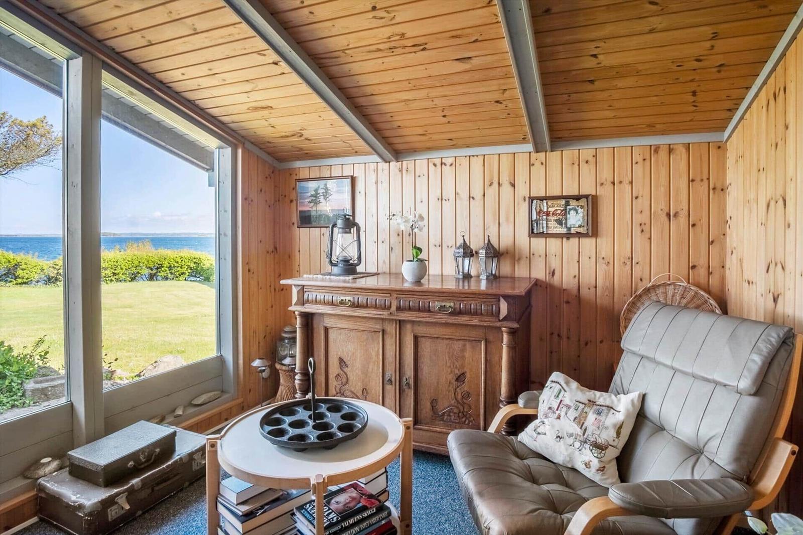 Room with wooden walls and ceiling, seating, table, and window with view of water.