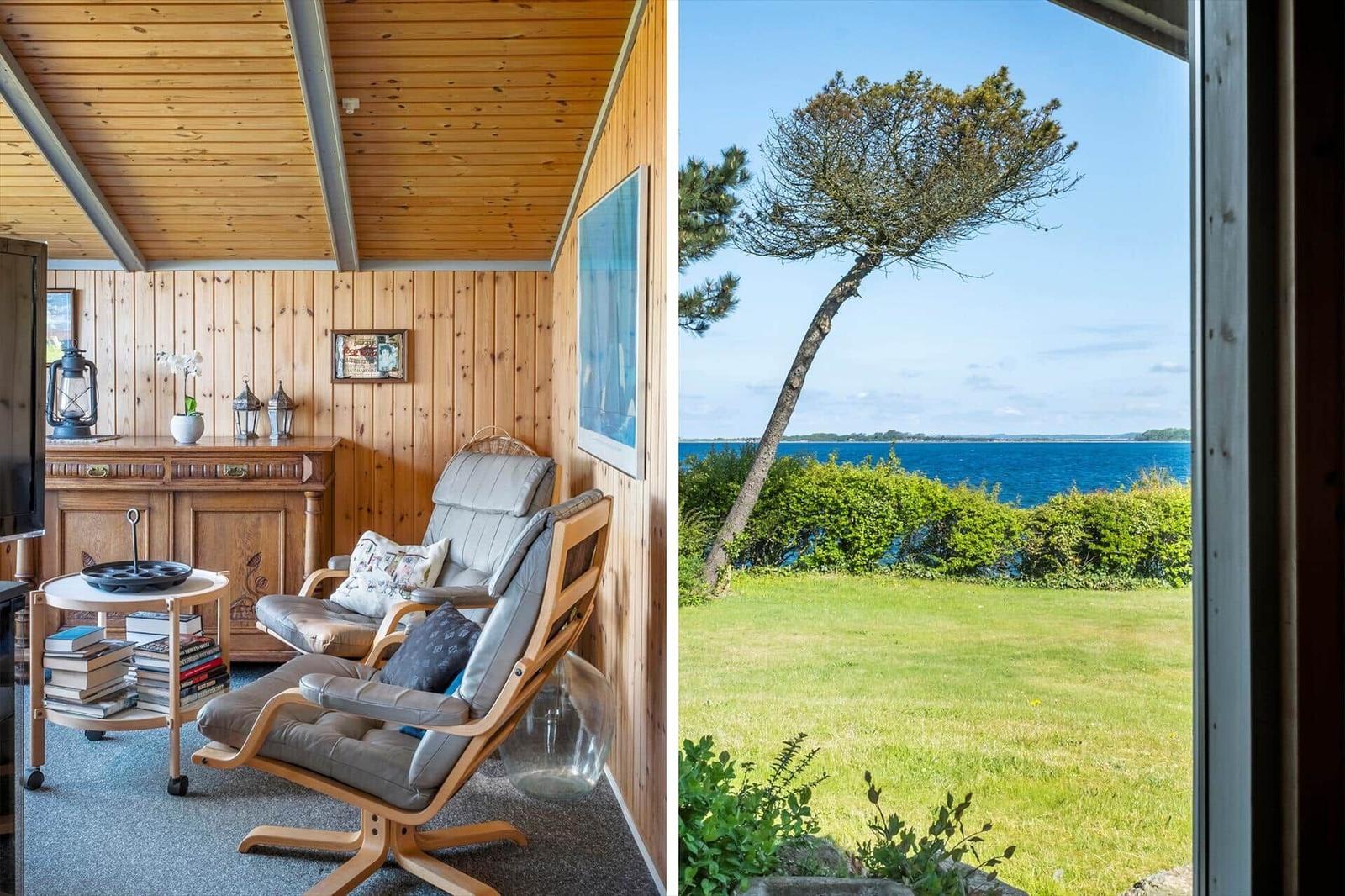 Living area with wooden walls and chairs. View of green lawn and sea.