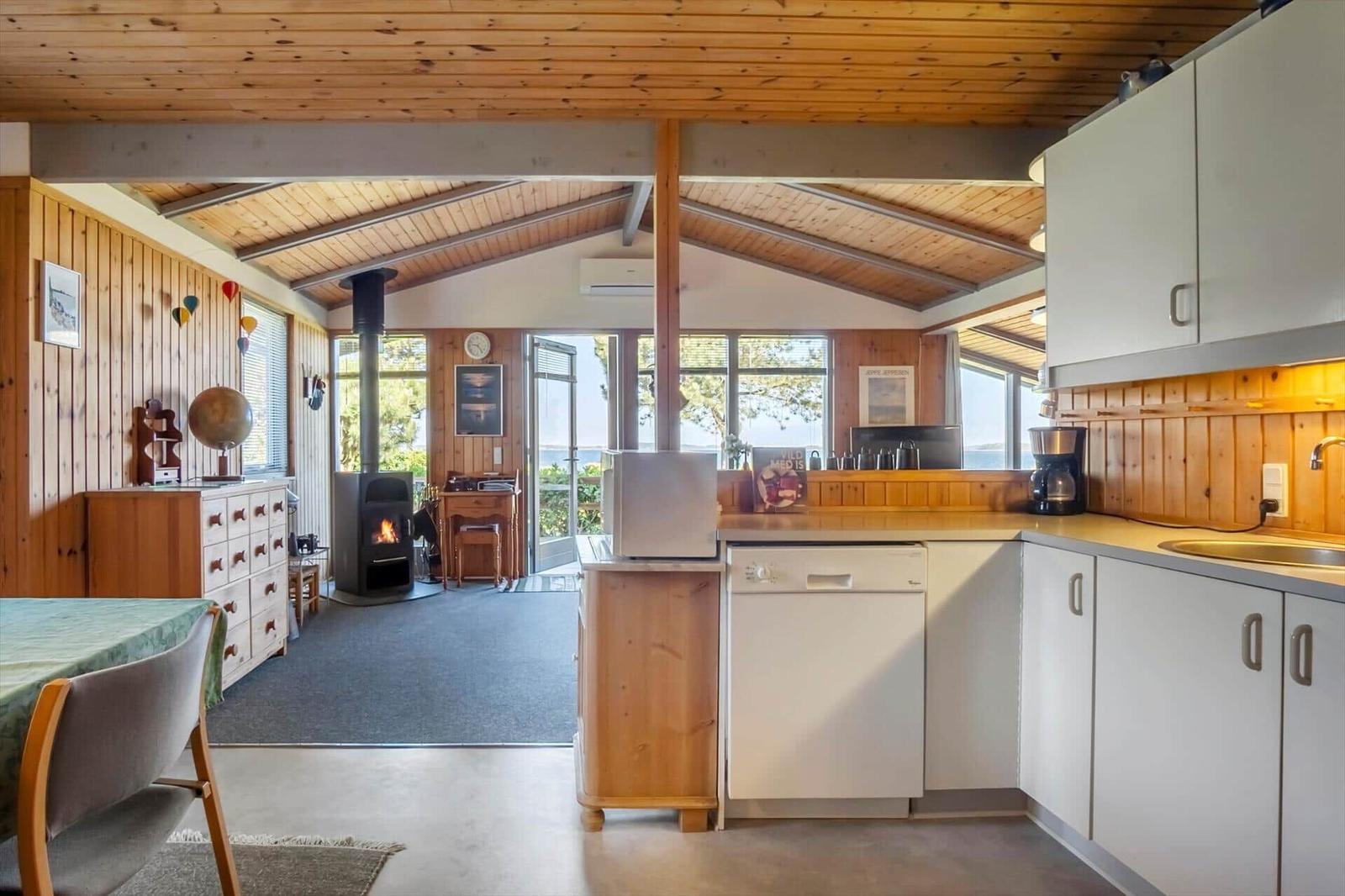 Kitchen with sink and dishwasher, living area with fireplace and wood wall
