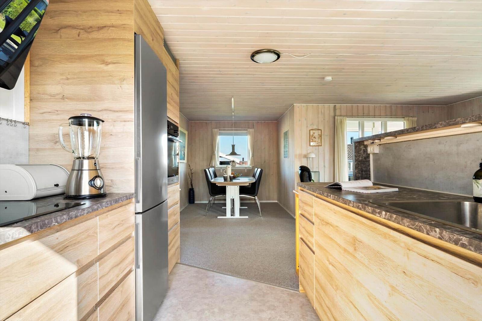 Küche mit Holzelementen, Kühlschrank und Esstisch im Hintergrund.
