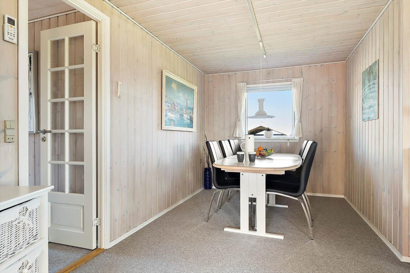Esszimmer mit Tisch, Stühlen und Fenster. Holzwände und Bodenbelag.