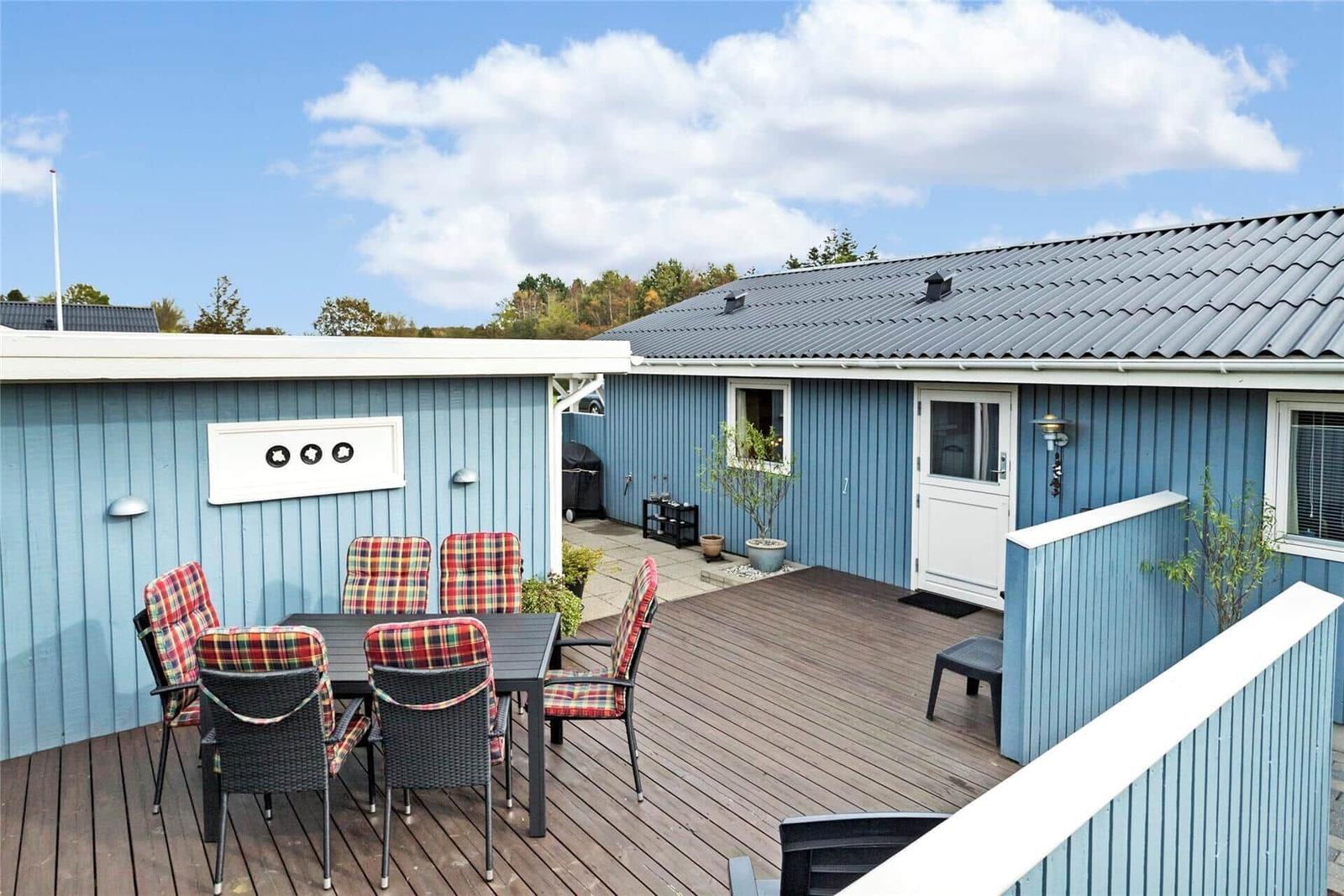 Terrasse mit Tisch und Stühlen vor einem blauen Haus mit Holzdecke.