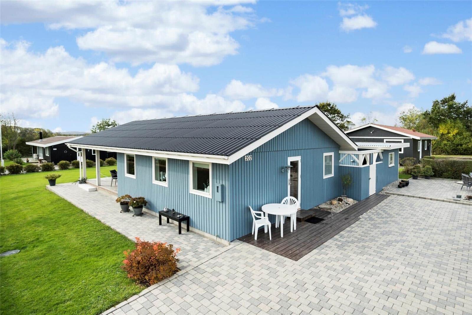 Blau gestrichenes Ferienhaus mit Terrasse und Garten. Weiße Möbel und gepflasterte Fläche.